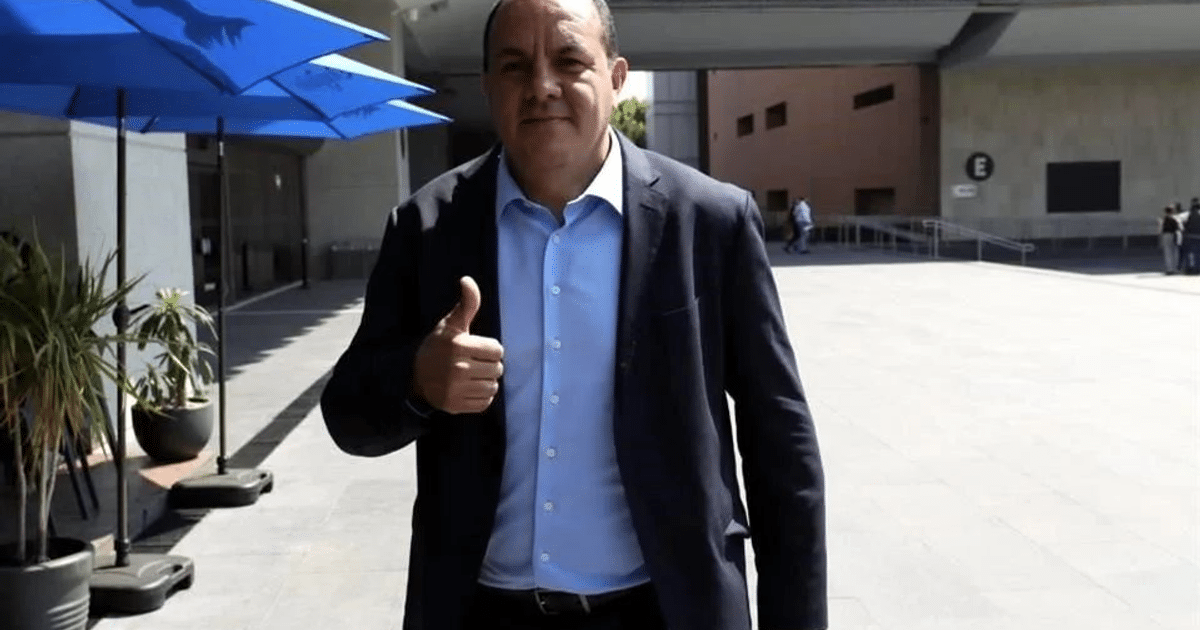 Hombre sonriente con pulgar arriba y sombrillas azules en fondo urbano