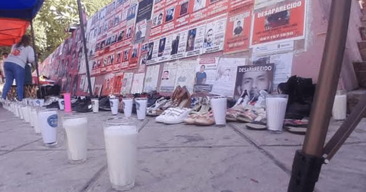 Mural con carteles de desaparecidos, zapatos y vasos de leche en evento de protesta.