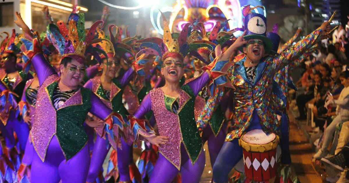 Personas en trajes coloridos desfilando en el Carnaval “La Perla” de Mazatlán, con un ambiente festivo y alegre.