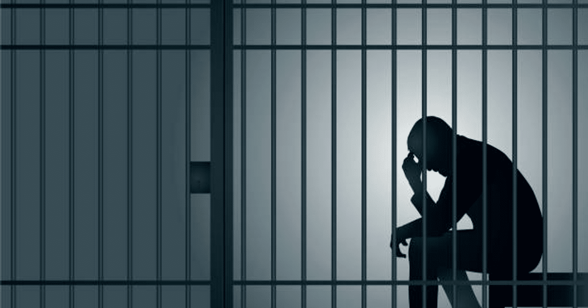 Silueta de una persona reflexionando en una celda de prisión, con barras visibles y luz tenue, evocando aislamiento.