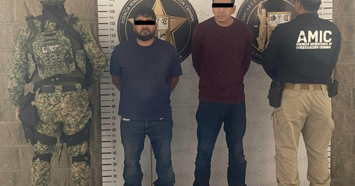 Dos personas esposadas frente a una pared de una agencia de investigación criminal, custodiadas por un agente de seguridad en uniforme militar.