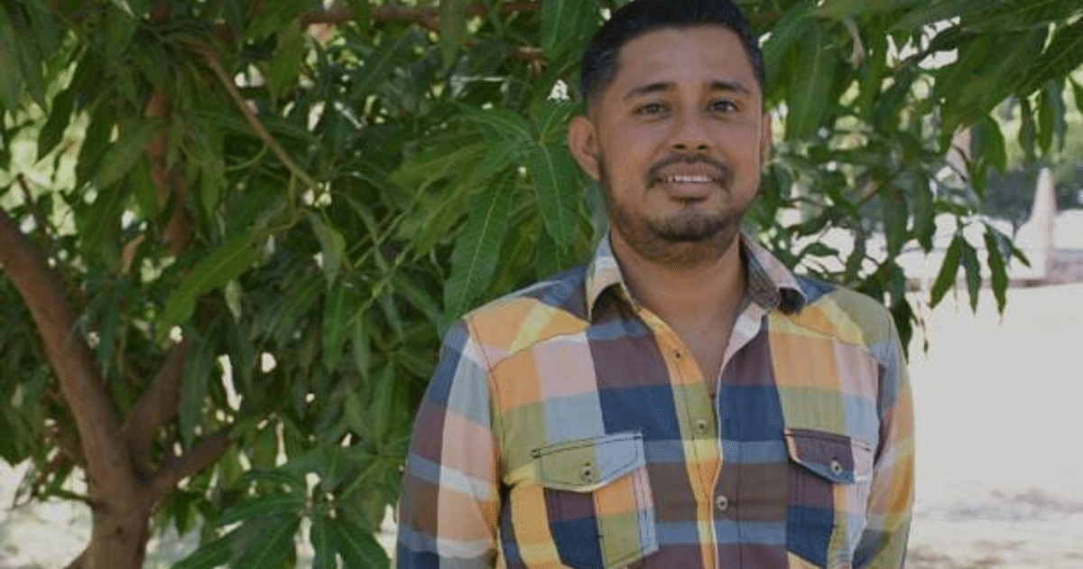 Profesor Juan Fernando Sánchez Rodríguez en un entorno natural con hojas verdes y un árbol.