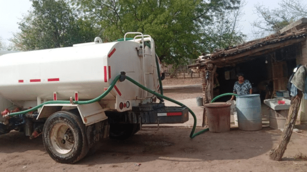 Camión cisterna blanco suministrando agua en una comunidad rural de Concordia, con mangueras conectadas a tanques y una mujer supervisando.