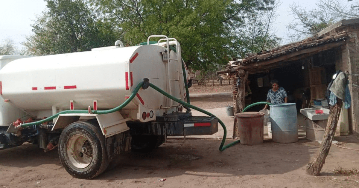 Camión cisterna blanco suministrando agua en una comunidad rural de Concordia, con mangueras conectadas a tanques y una mujer supervisando.