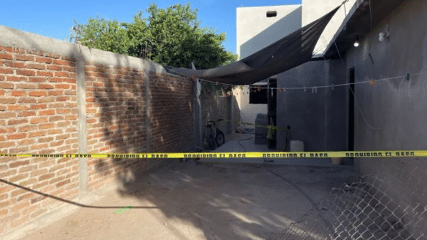 Callejón con pared de ladrillo, bicicleta, tendedero y cinta de advertencia amarilla.
