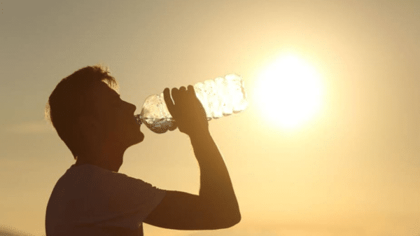 Silueta de persona bebiendo agua al amanecer con el sol de fondo