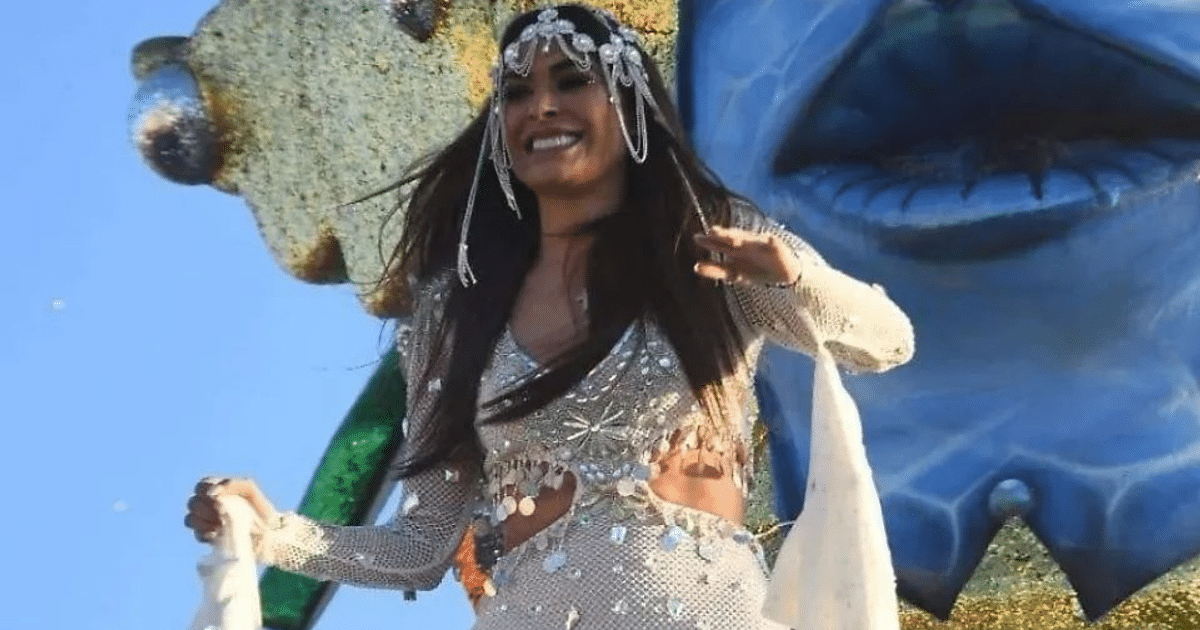 Mujer sonriente en atuendo brillante en un evento festivo con decoración colorida de fondo.