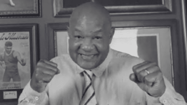Persona sonriendo y haciendo un gesto de lucha frente a cuadros enmarcados, evocando a George Foreman.