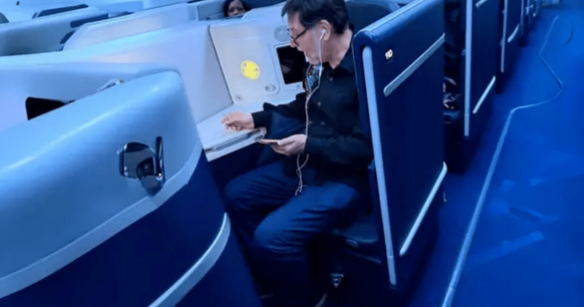 Pasajero en clase ejecutiva de avión, usando auriculares y dispositivo móvil, con diseño moderno y cómodo.