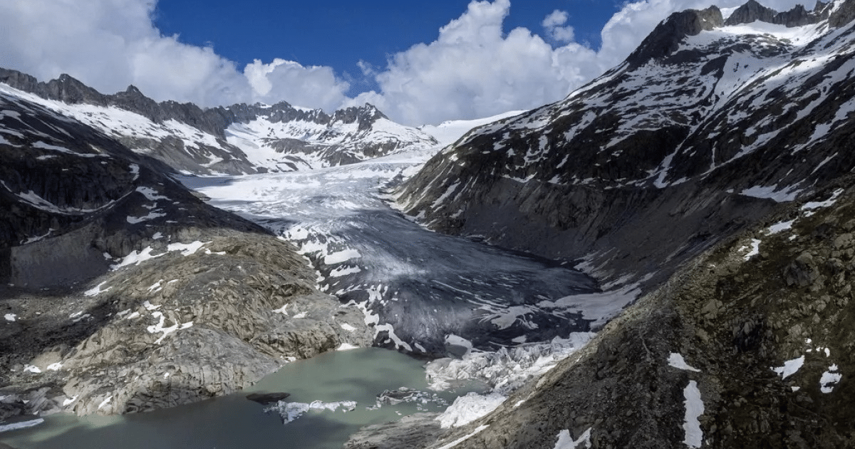 Vista del glaciar Aletsch rodeado de montañas nevadas y un lago verde esmeralda bajo un cielo parcialmente nublado.