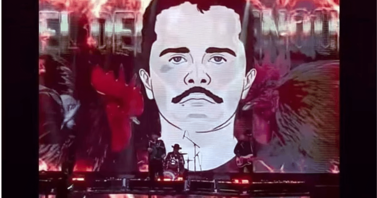 Hombre con bigote en fondo colorido durante concierto con músicos en el escenario.