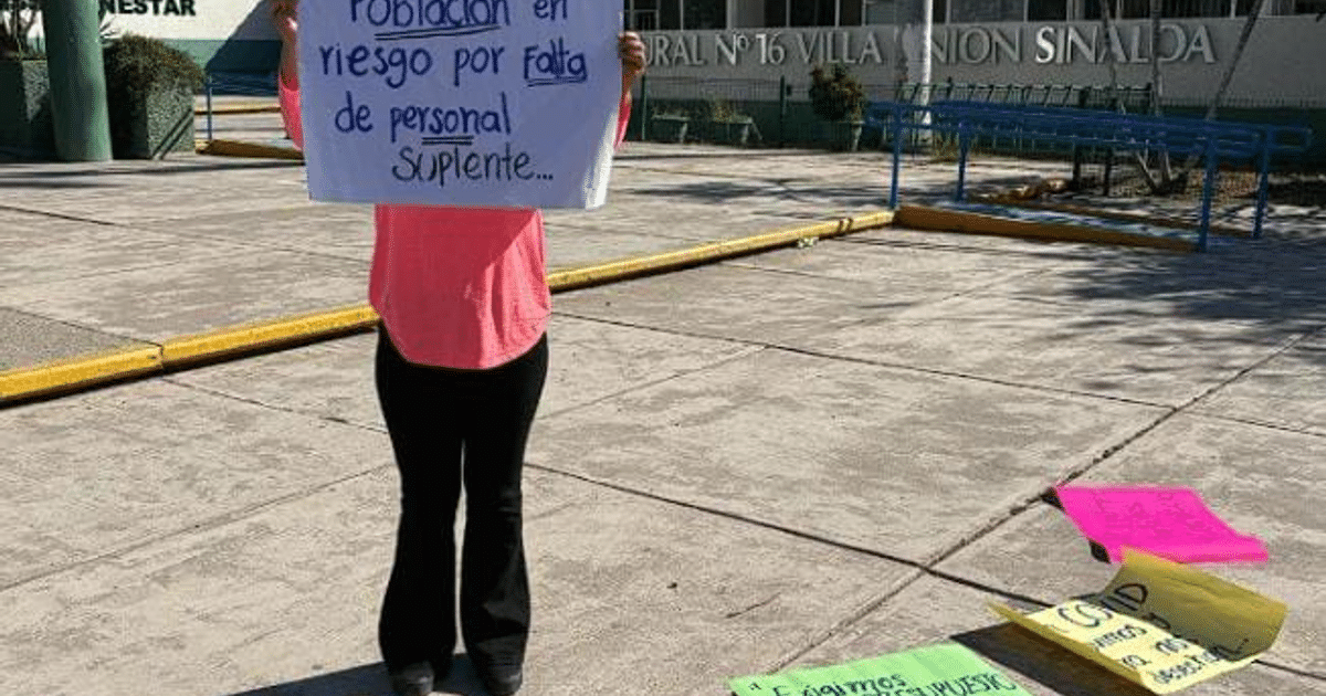 Persona sosteniendo un cartel en protesta del IMSS Bienestar en Villa Unión, con carteles de colores en el suelo.