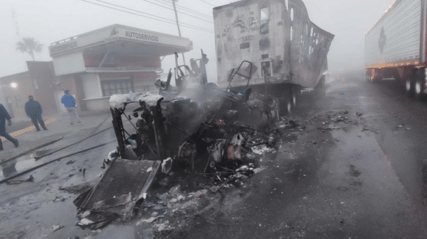Camión dañado por incendio en zona industrial de Los Mochis, con humo y personas alrededor.