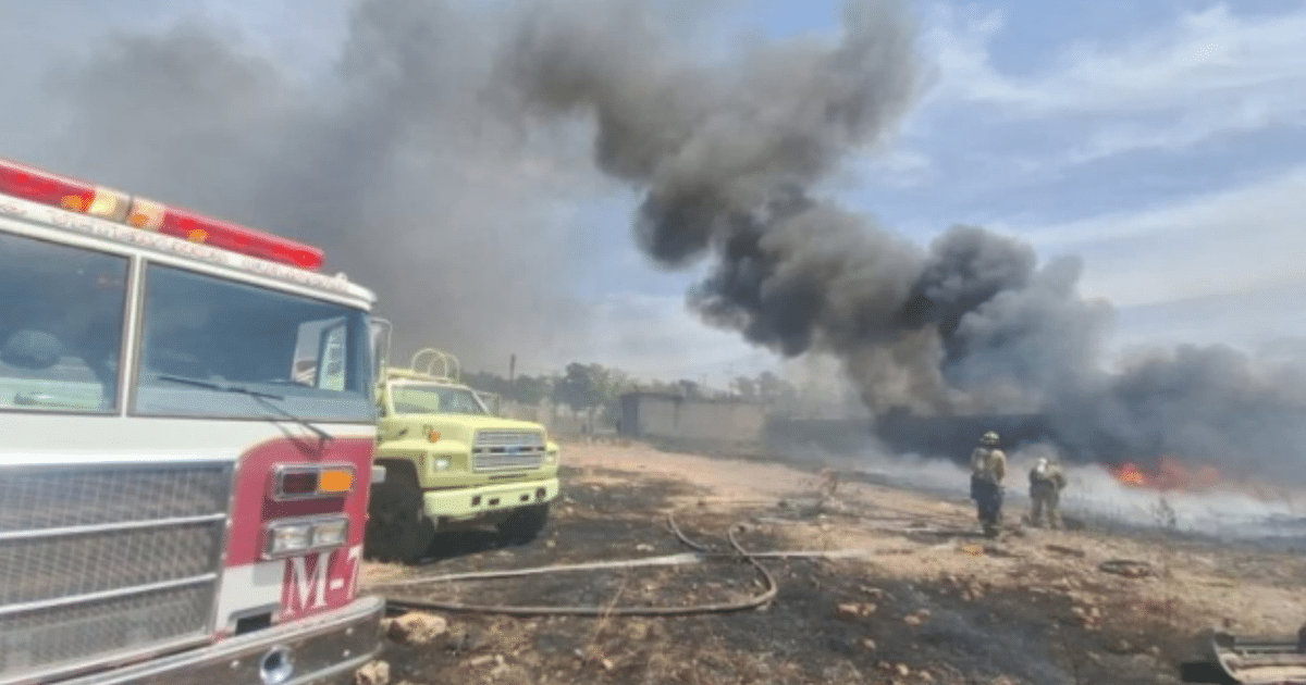 Camión de bomberos y vehículo amarillo en un incendio en Culiacán, con humo y llamas al fondo.