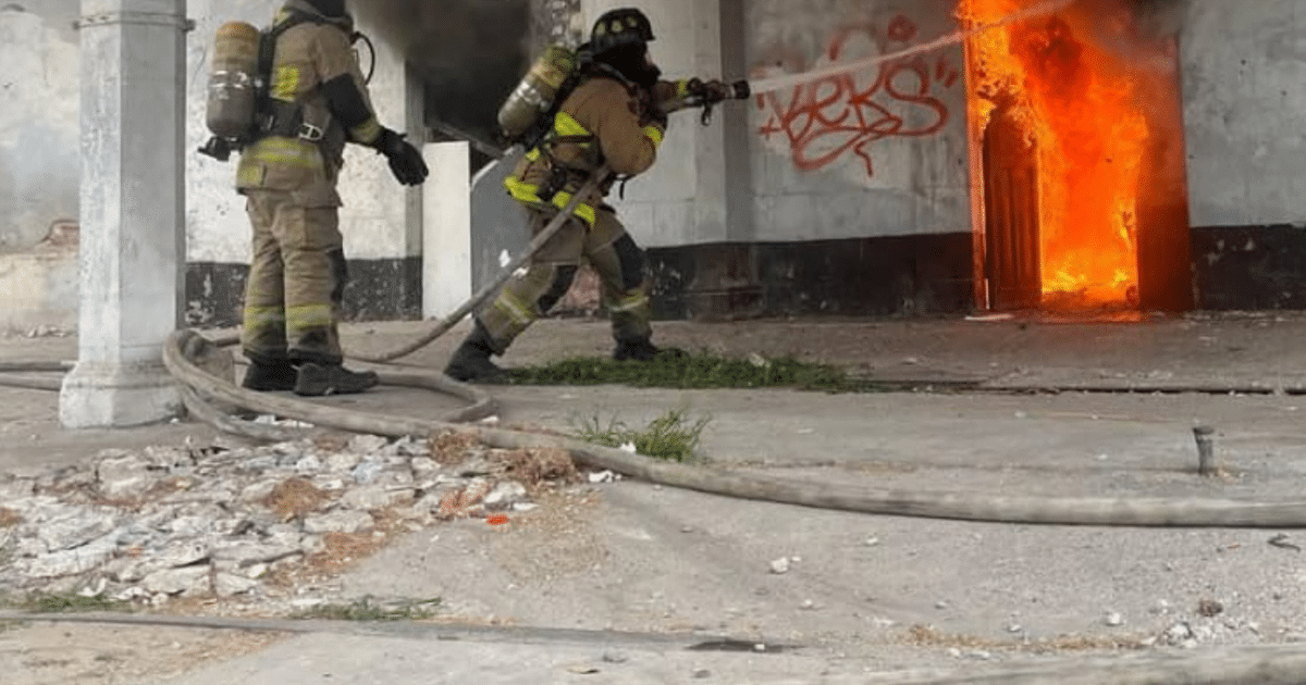 Bomberos combatiendo incendio en Mazatlán, con fuego y humo saliendo de una puerta en un entorno urbano.