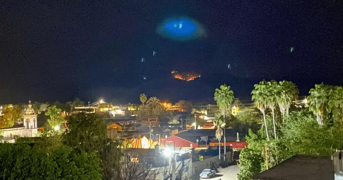 Vista nocturna de Mazatlán con actividad volcánica en el fondo y luces urbanas.