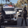 Dos policías armados frente a un vehículo policial en una calle urbana con palmeras, en Mazatlán.