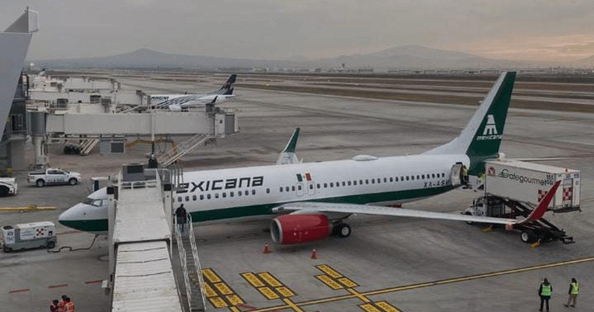 Avión de Mexicana en pista de aeropuerto con cielo nublado y personal trabajando.