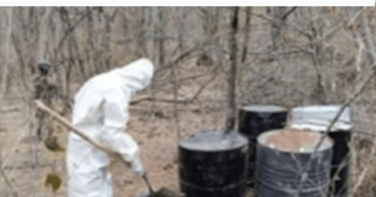 Agente en traje de protección en operativo antidroga en Sinaloa, con tambos negros en un entorno forestal.