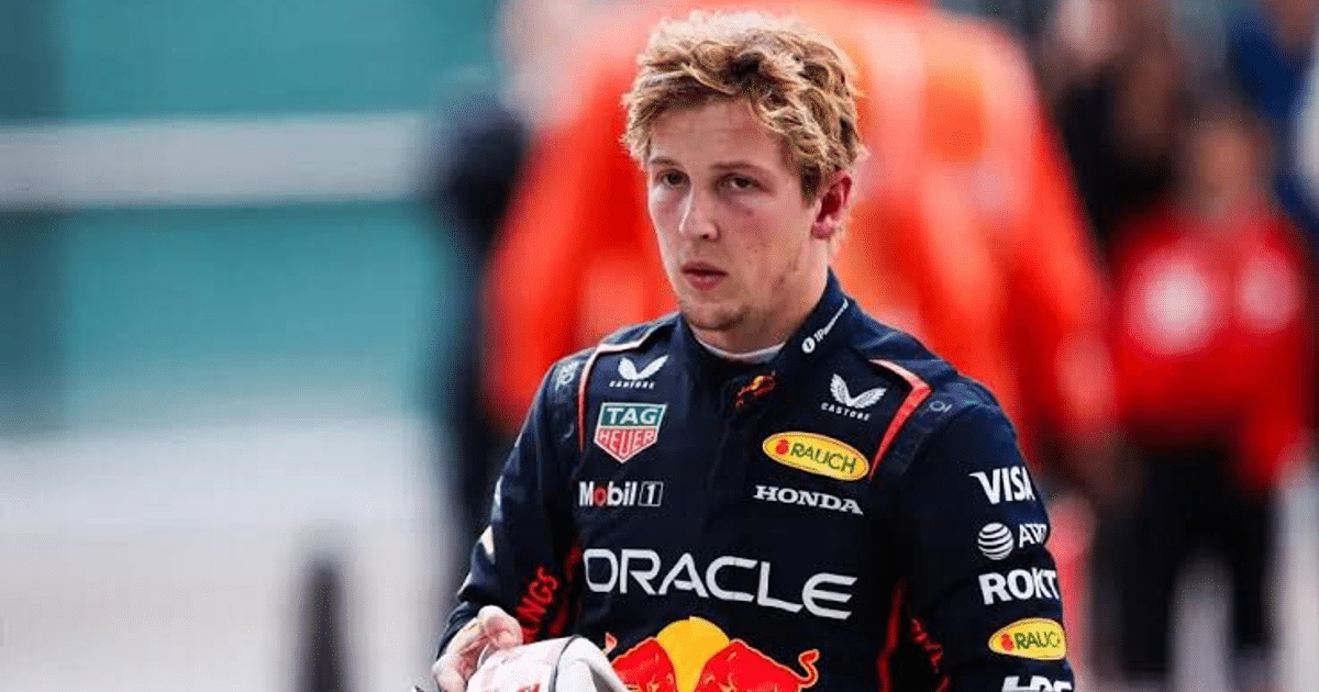 Piloto de Fórmula 1 con traje de competición en un evento, rodeado de personas y objetos relacionados con la carrera.