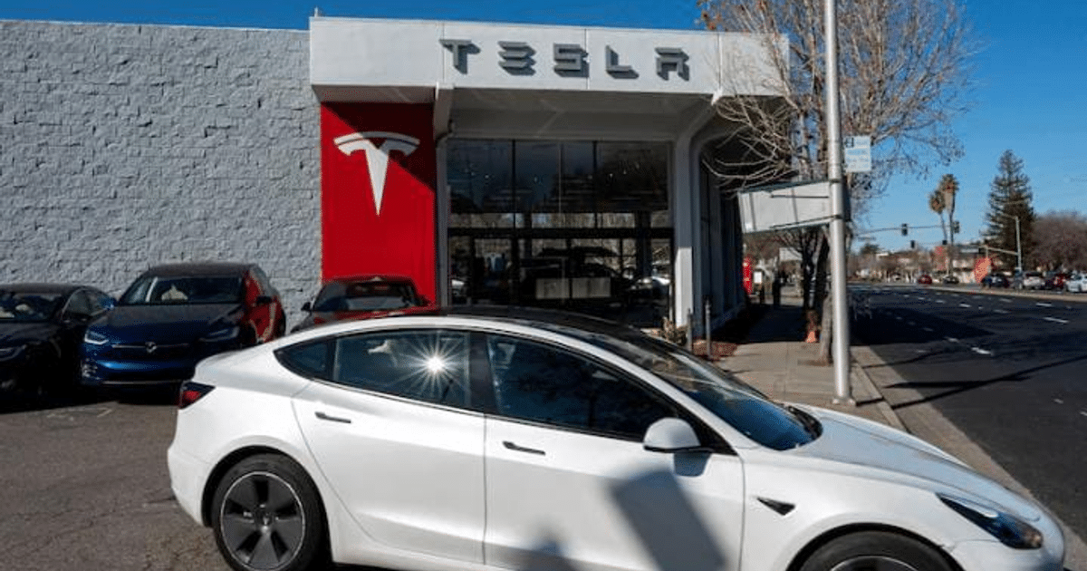 Concesionario Tesla con coche blanco aparcado y logotipo en la pared, en un día despejado.