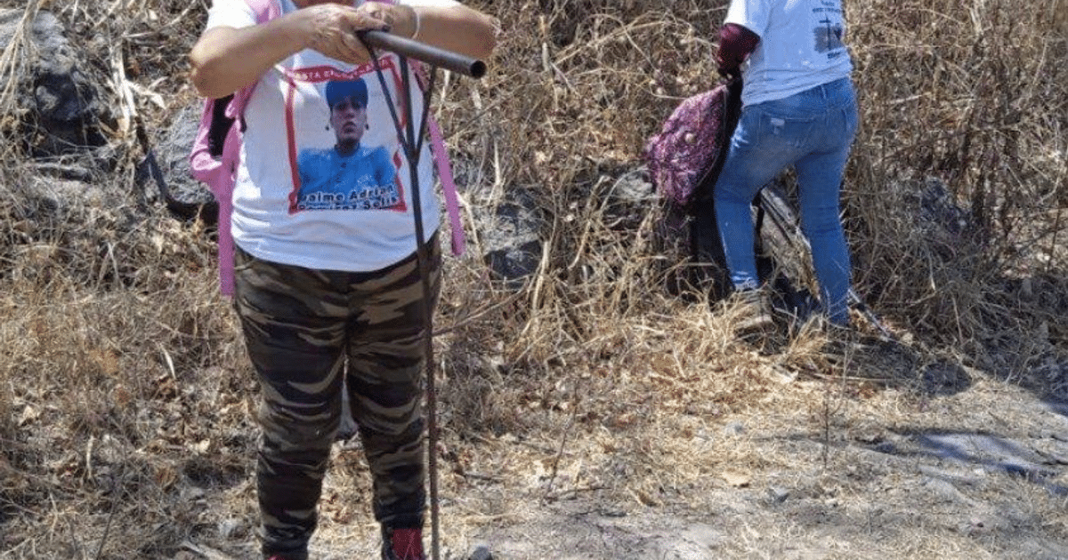 Dos personas en ambiente árido: una con camiseta estampada y pantalones de camuflaje, y otra de espaldas con camiseta blanca, reflejando la vulnerabilidad de activistas en Jalisco.