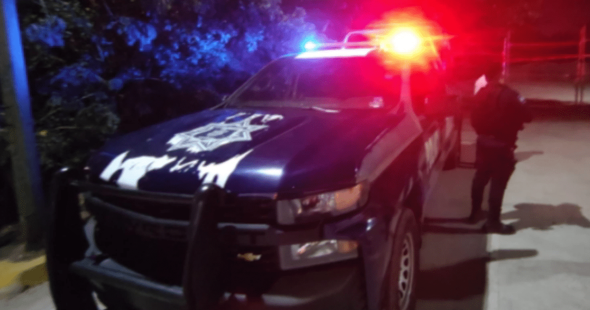 Camioneta de policía con luces encendidas en Mazatlán durante la noche, con un agente de pie al lado.