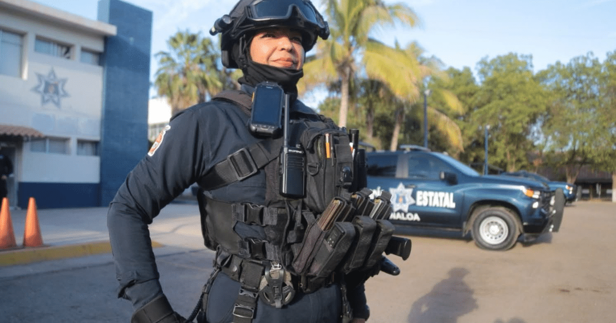 Comandante de la Policía Estatal con chaleco táctico frente a un vehículo policial en una estación.