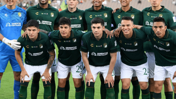 Jugadores de fútbol con camisetas verdes y pantalones cortos blancos posan para una foto de equipo, con un portero en uniforme azul a la izquierda.