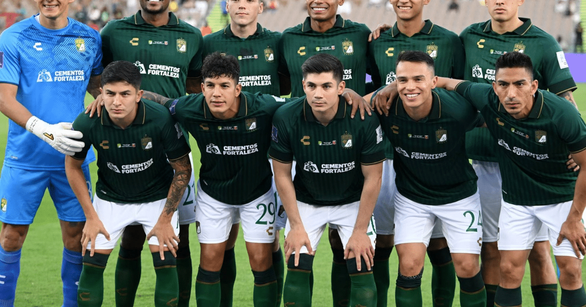 Jugadores de fútbol con camisetas verdes y pantalones cortos blancos posan para una foto de equipo, con un portero en uniforme azul a la izquierda.