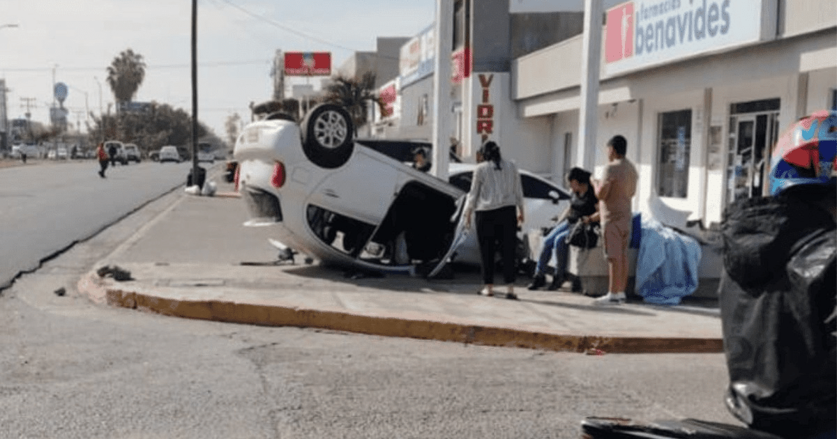 Automóvil Nissan March blanco volcado en Mazatlán, rodeado de personas en una vía pública.