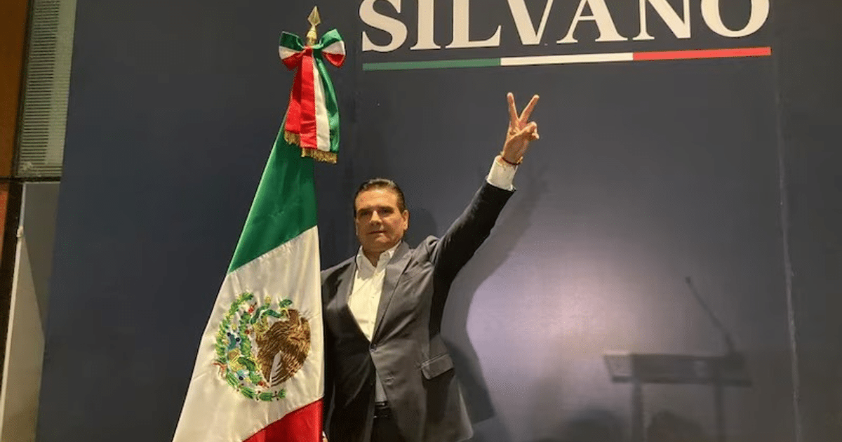 Persona haciendo gesto de victoria junto a bandera mexicana con fondo de 'SILVANO'.