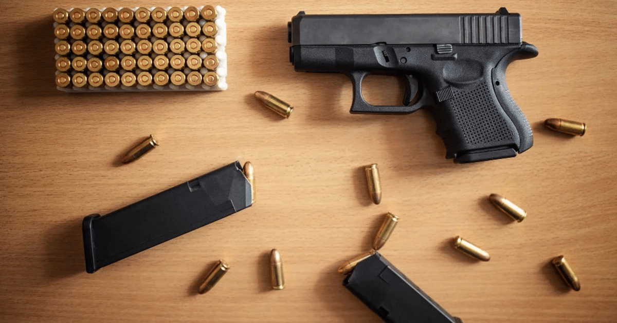 Pistola negra con cartuchos de bala y cargador sobre madera