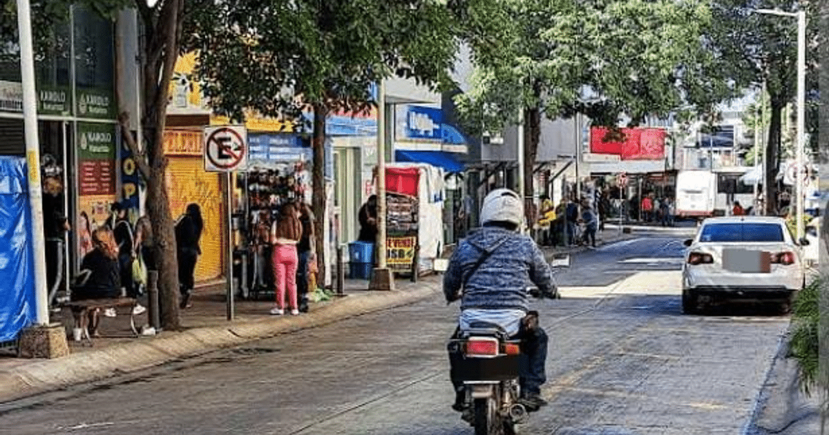 Calle urbana en Culiacán con vehículos, motociclista, tiendas y árboles durante la reactivación económica.