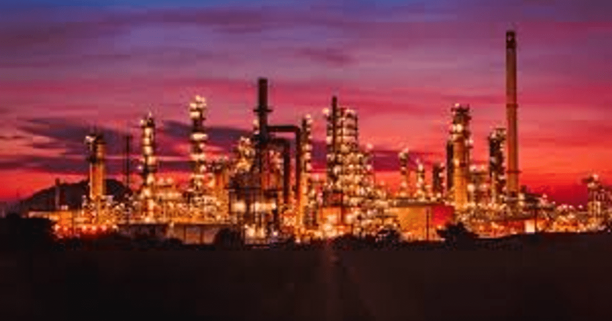 Refinería industrial iluminada al atardecer con cielo naranja y púrpura, relacionada con la suspensión de compras de crudo venezolano por aranceles.
