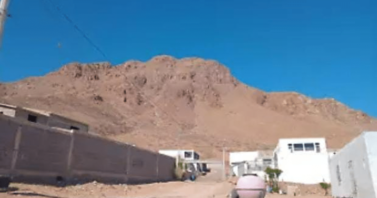 Vista del Cerro Grande con montaña rocosa y edificaciones en primer plano, cielo azul despejado.