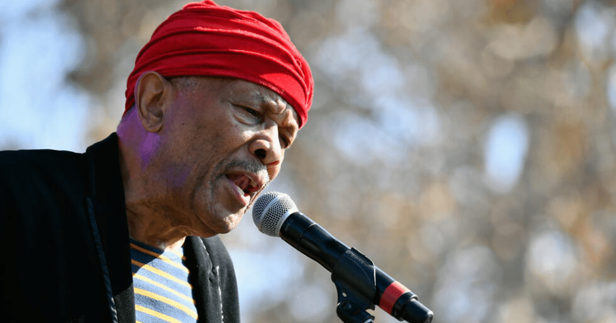 Hombre cantando con gorro rojo y camiseta a rayas en evento al aire libre
