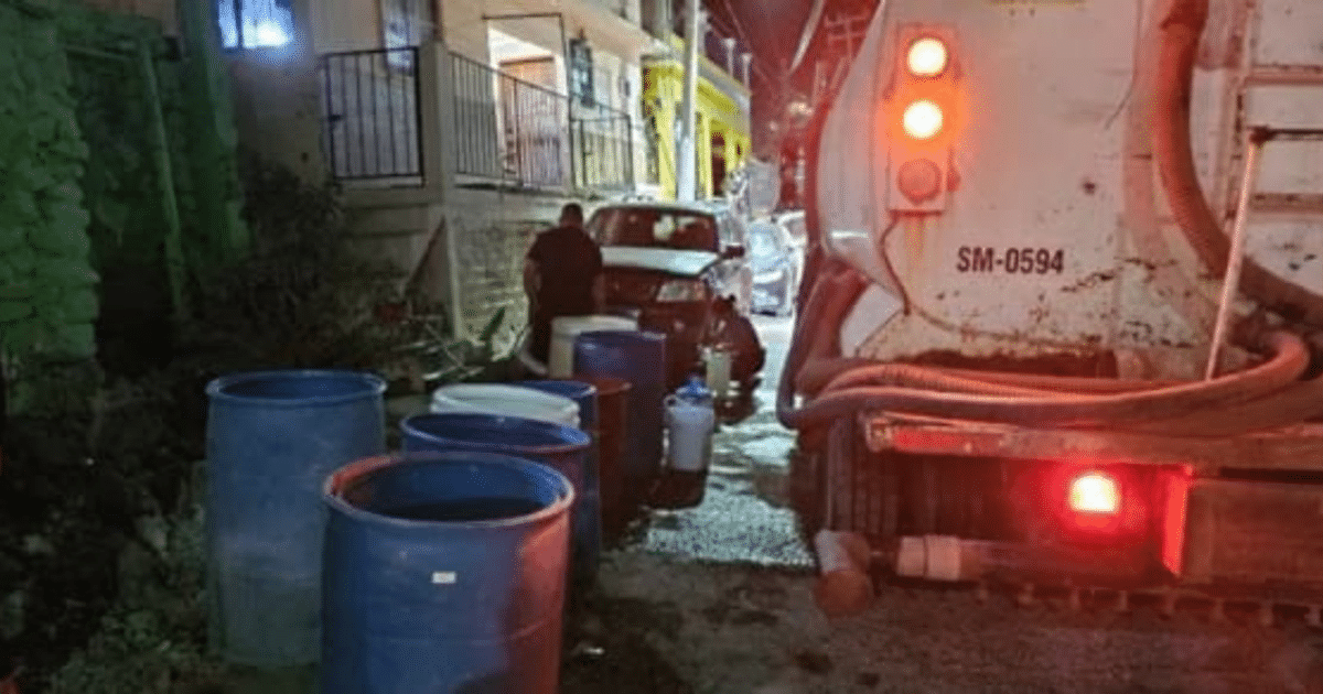 Camión de basura en callejón con barriles azules durante crisis de agua en Topolobampo