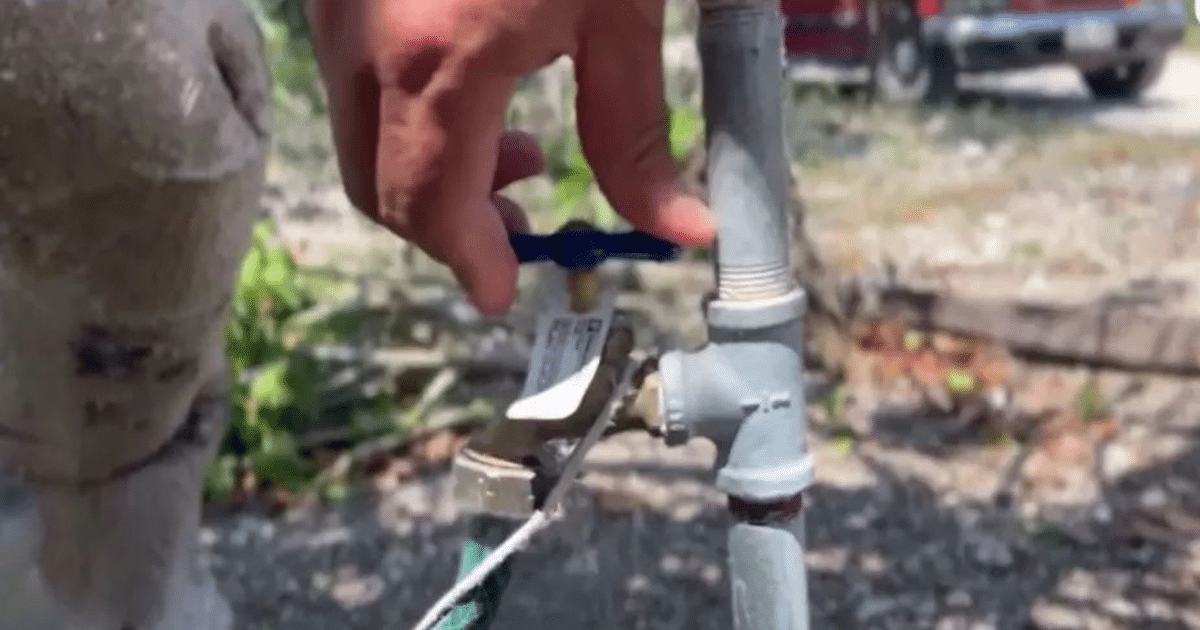 Mano ajustando una válvula de agua metálica al aire libre, relacionada con la gestión hídrica en Sinaloa.