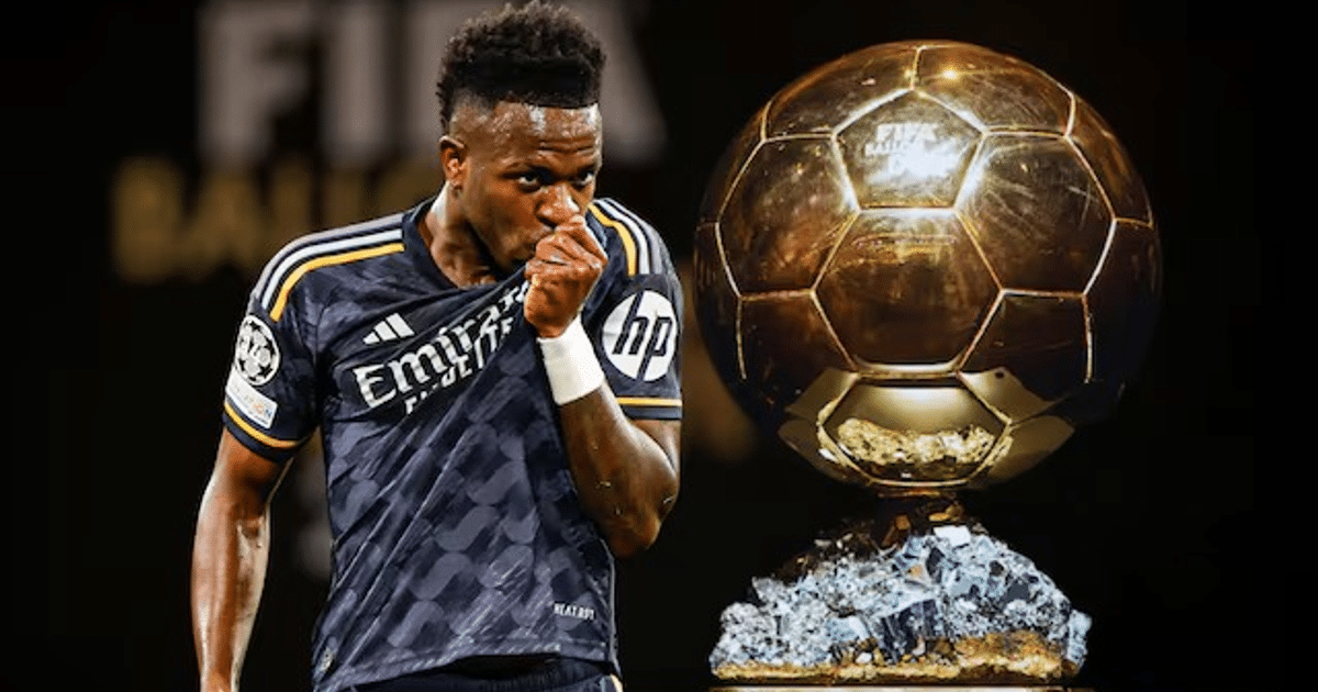 Vinicius Junior mostrando su camiseta junto a un trofeo de fútbol en un fondo oscuro.