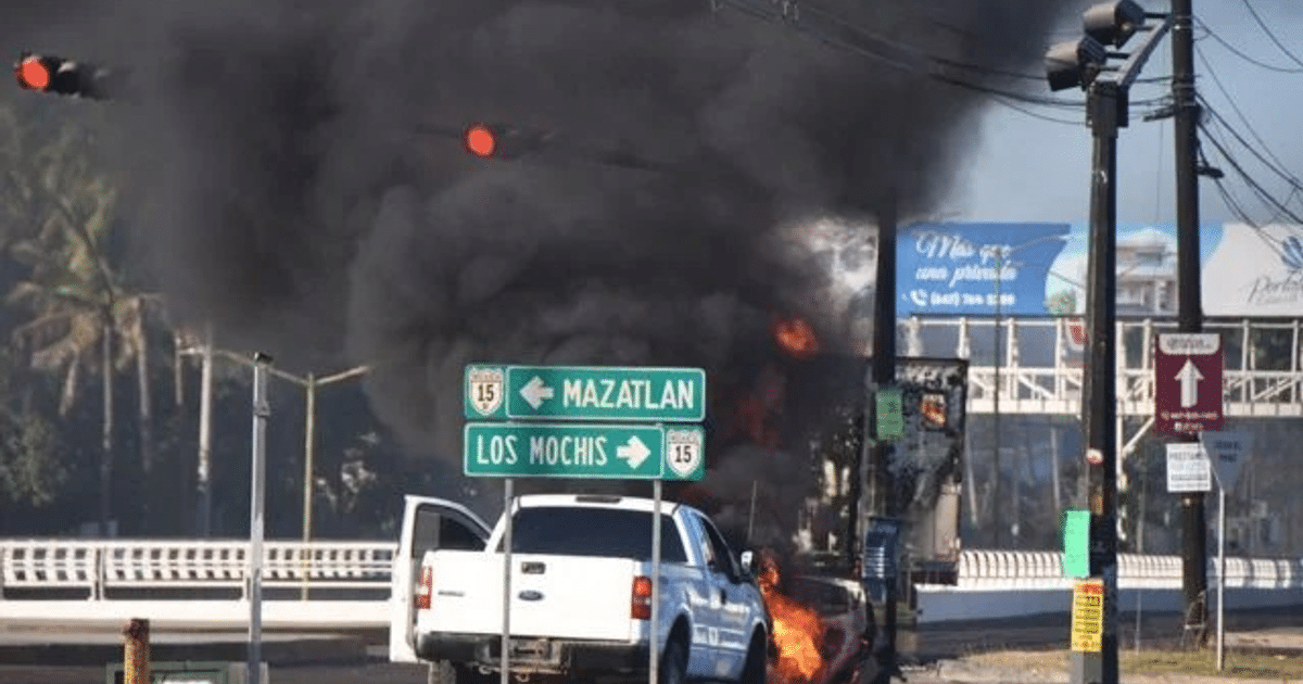 Vehículo en llamas en Sinaloa con señales de tráfico hacia Mazatlán y Los Mochis, humo negro y semáforo en rojo.