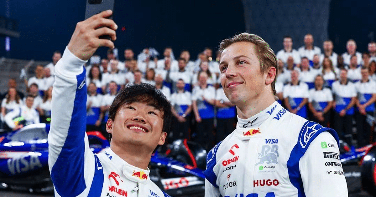 Pilotos de Red Bull en Suzuka posando para un selfie con el equipo y coche de carreras al fondo.