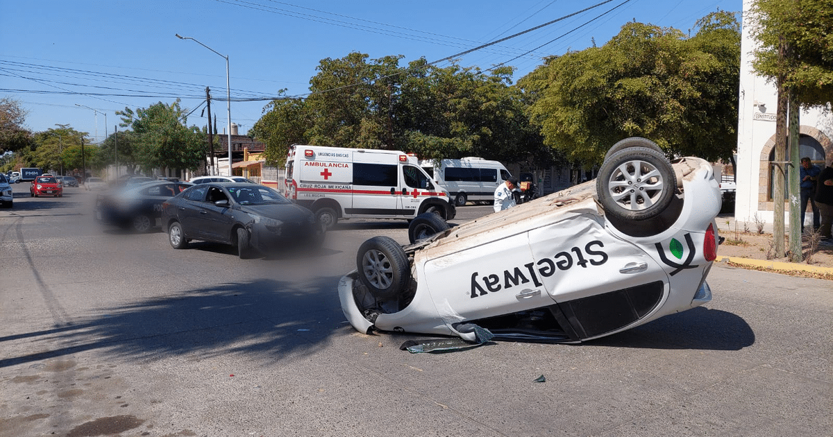 Coche volcado en accidente vial en Los Mochis con ambulancia y personal de emergencia presentes.