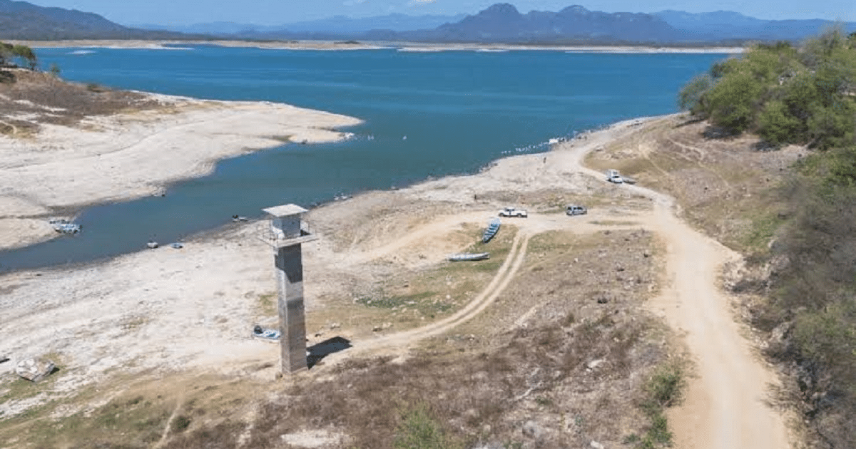 Vista de un lago en Sinaloa con torre de monitoreo, caminos y montañas al fondo.