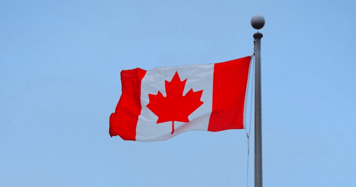 Bandera de Canadá con franjas rojas y hoja de arce roja sobre fondo blanco, cielo despejado