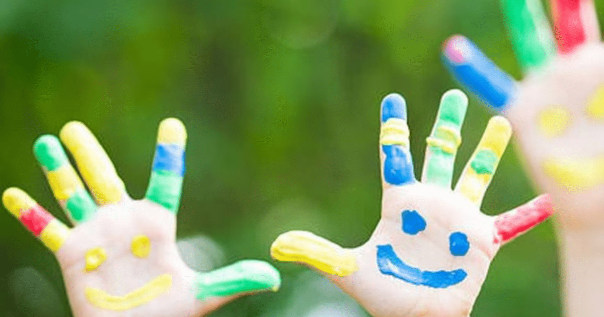 Manos pintadas con colores brillantes y caras sonrientes en un entorno natural.