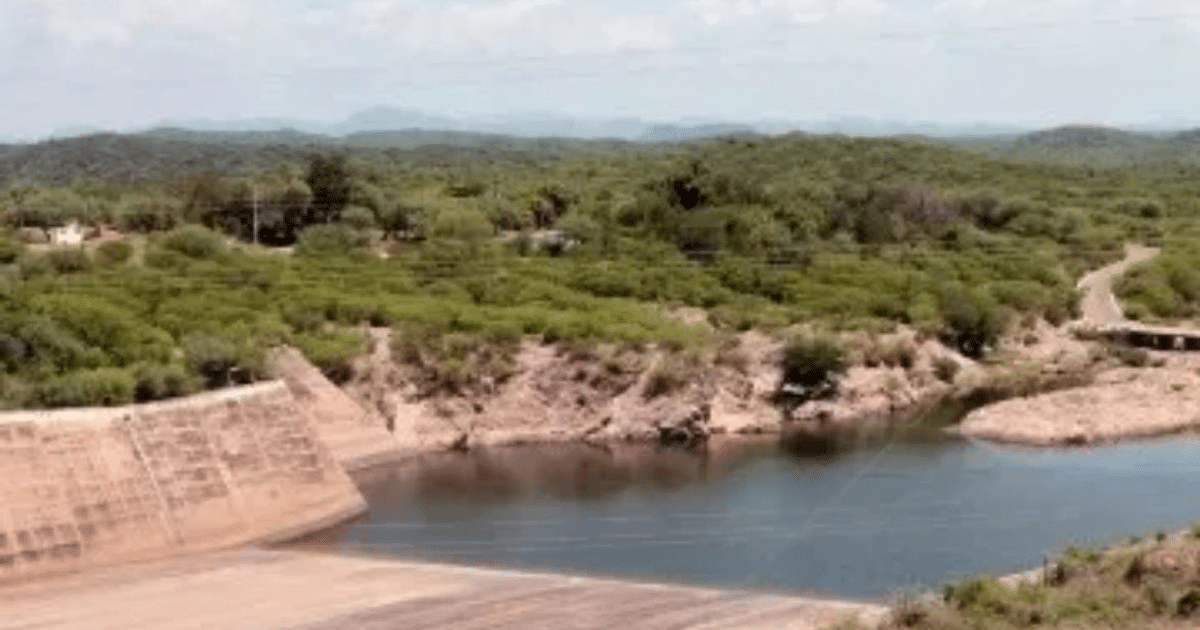 Embalse en Sinaloa rodeado de vegetación y montañas, con un camino al lado del agua.
