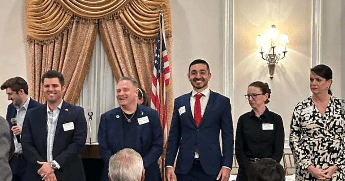 Personas en un evento político en Miami con una cortina dorada y bandera de EE.UU.