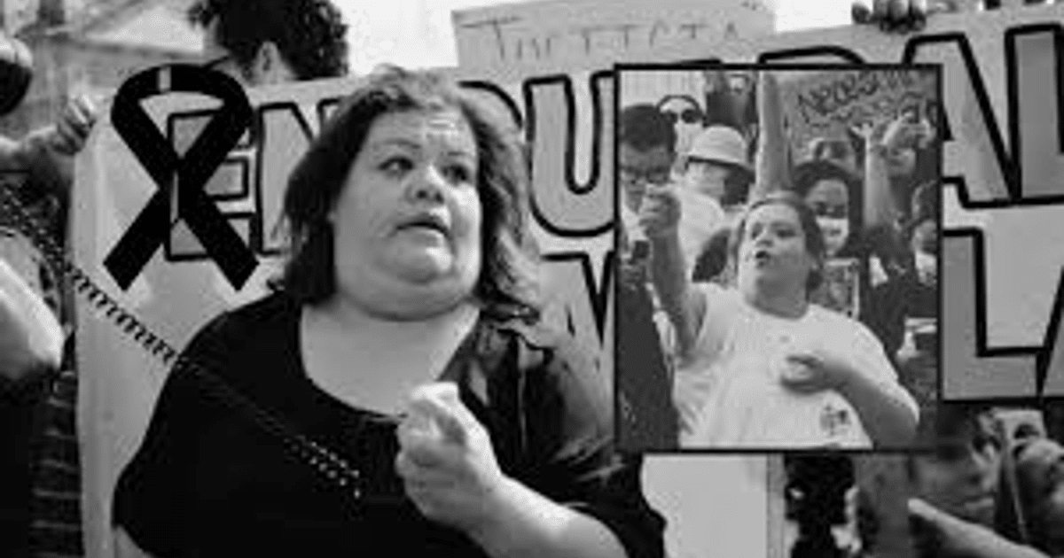 Mujer protestando en evento con lazo negro y cartel, en memoria de Teresa González Murillo, activista agredida en Guadalajara.