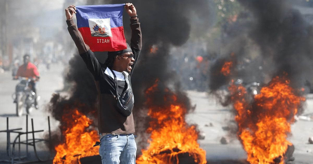 Hombre con bandera de Haití en protesta con llamas de fondo